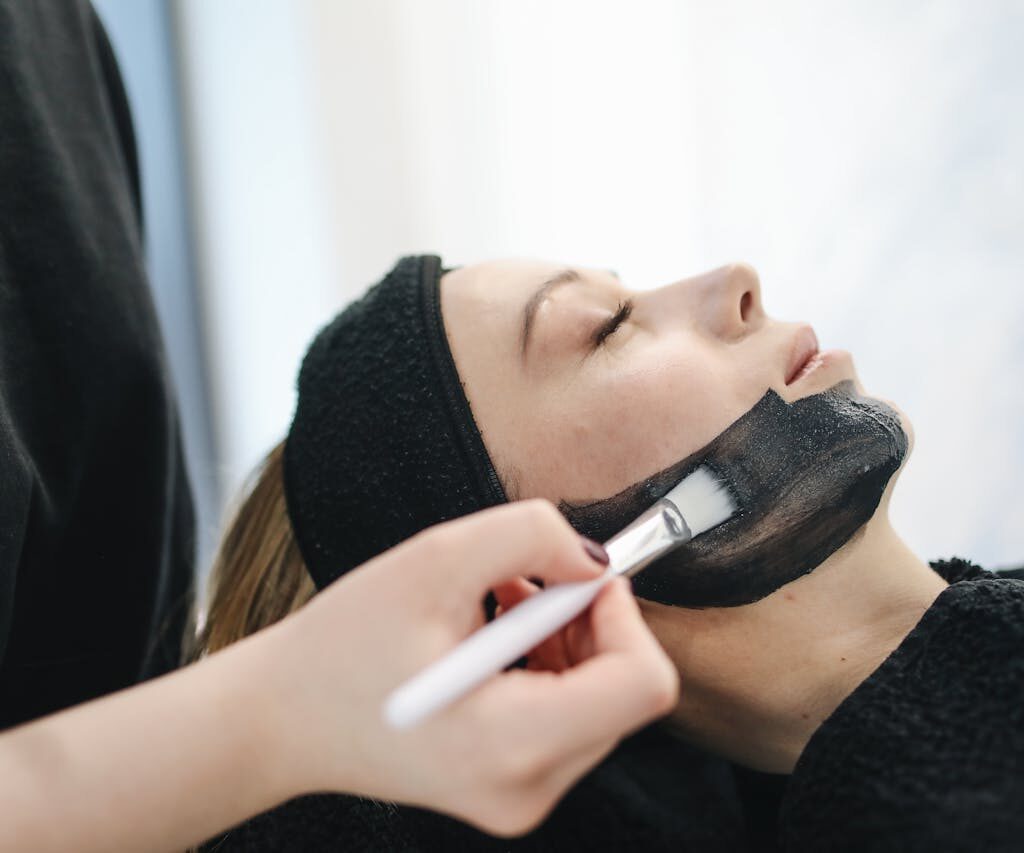 Close-up of a woman enjoying a relaxing charcoal facial treatment in a spa.