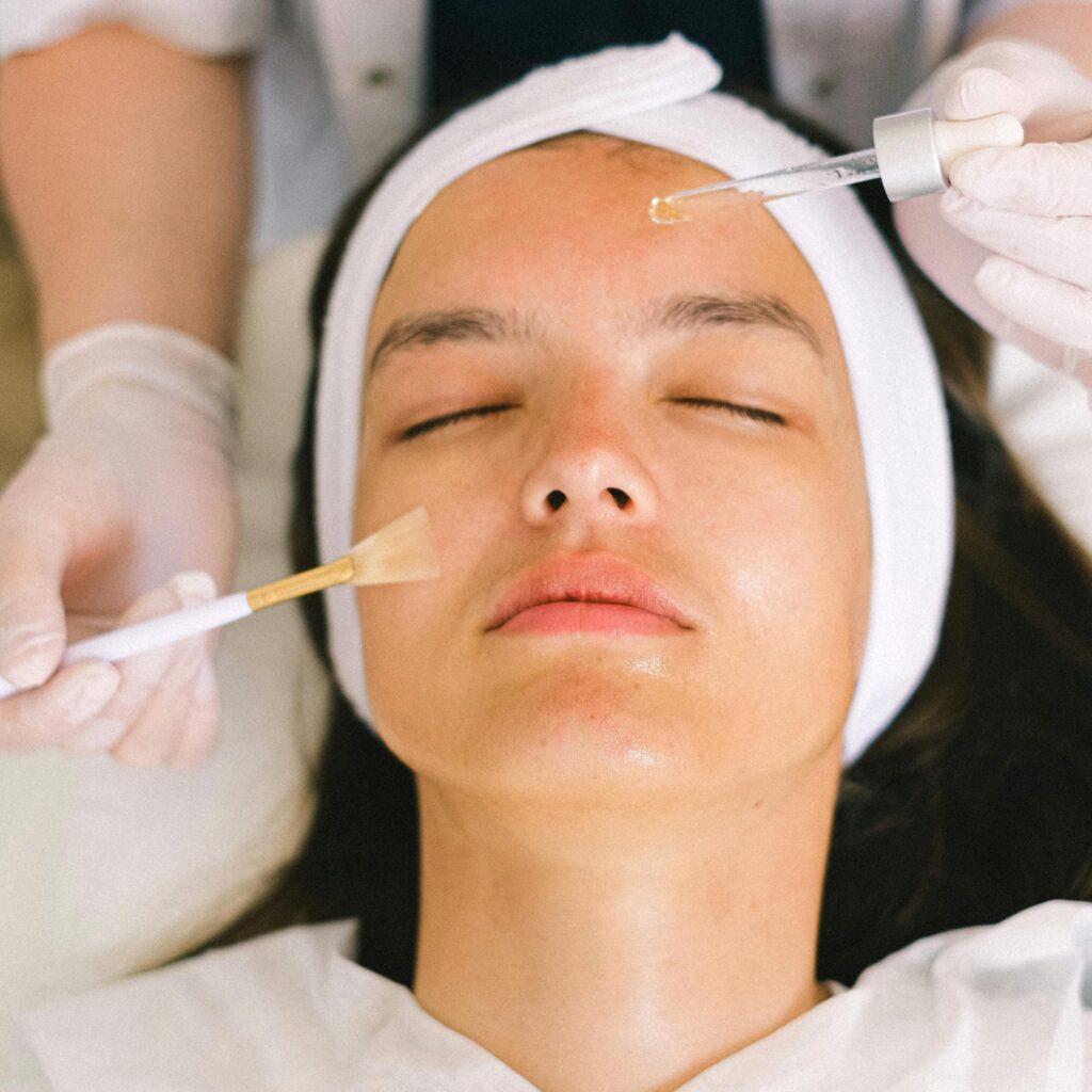 pexels-photo-5069432-5069432 Top view skilled female cosmetologist in uniform and gloves applying essential oil on young woman face skin while working in contemporary spa center